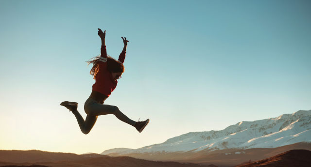 A girl jumps for joy in a mountain scene.