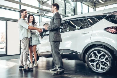 adult couple shopping for a car and shaking hands with car salesman next to brand new suv