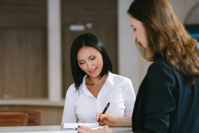 young adult female filling out paperwork with friendly female credit union representative