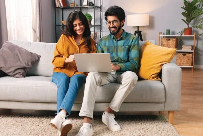 young married couple sitting together on couch looking at laptop computer